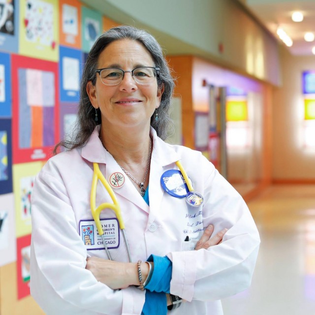 Jill C. Glick, MD, stands in hallway with children&#039;s drawings behind her