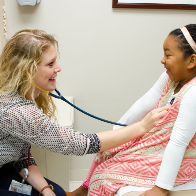 Physician laughing with a young patient while checking her heartbeat 