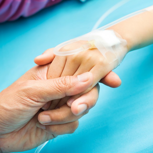 Adult holding the hand of a child with an IV