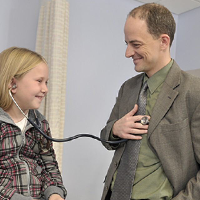 Siri Atma W. Greeley, MD, PhD laughing with a patient and letting her wear a stethoscope to check his heartbeat