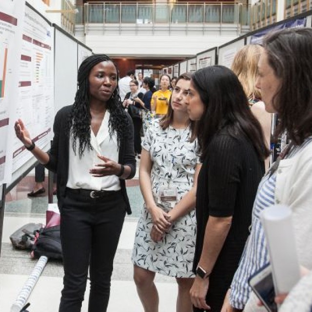 Researcher presenting a poster at a symposium to Nicola Orlov, MD, along with other doctors and researchers