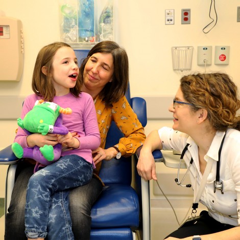 Patient sitting on her mom's lap and holding a plush Remoc while talking to her doctor